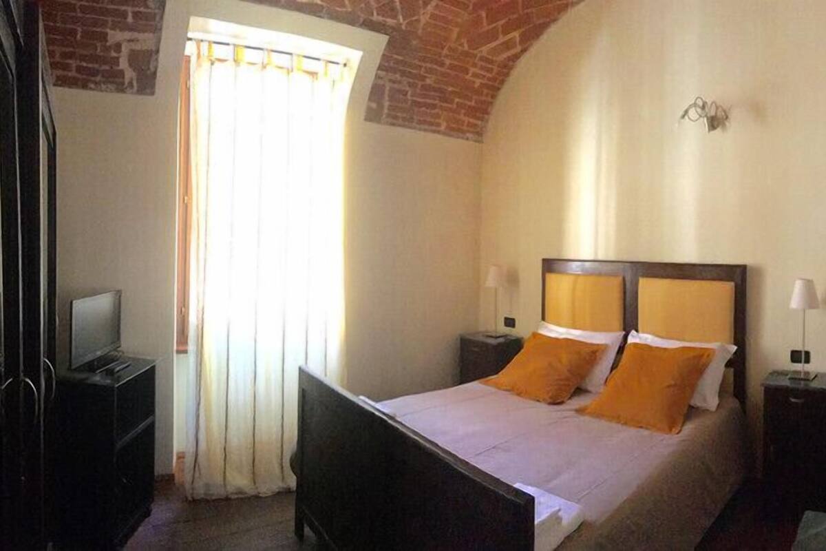 A bedroom with a bed, a TV, and a window with curtains.