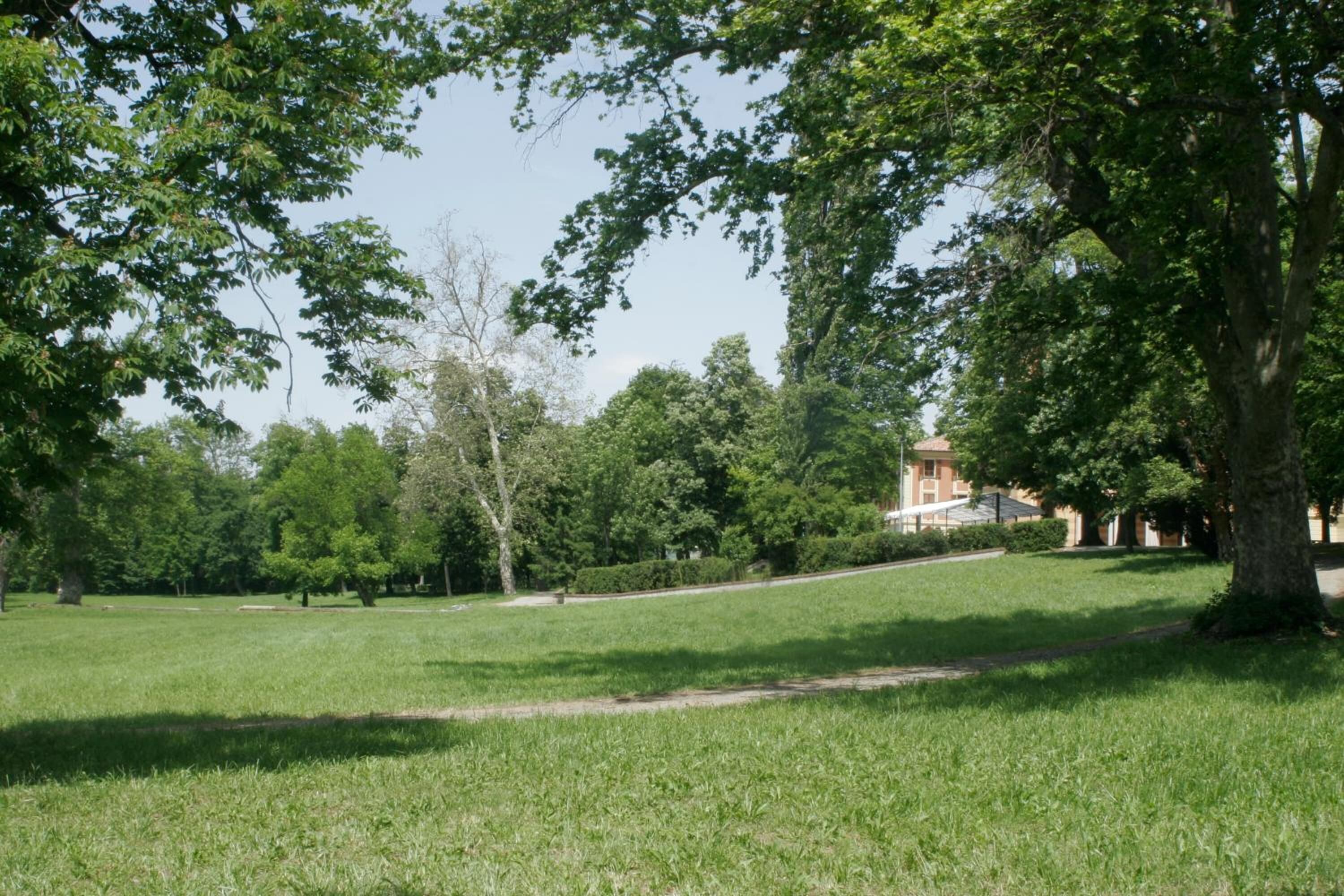 Un parc avec une zone herbeuse, des arbres et un bâtiment en arrière-plan.
