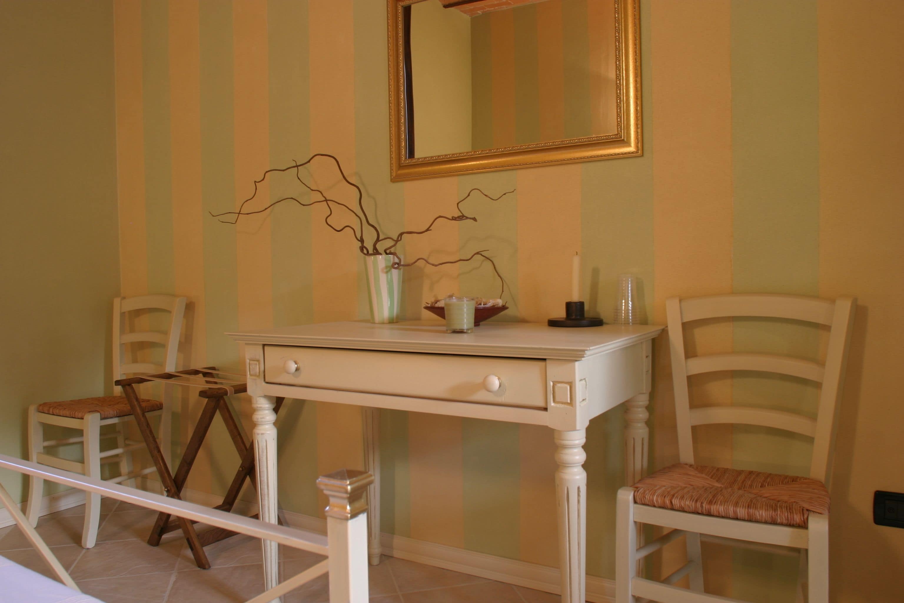 A room with a white vanity table, two chairs, a mirror, and a vase with branches.