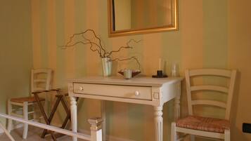 A room with a white vanity table, two chairs, a mirror, and a vase with branches.