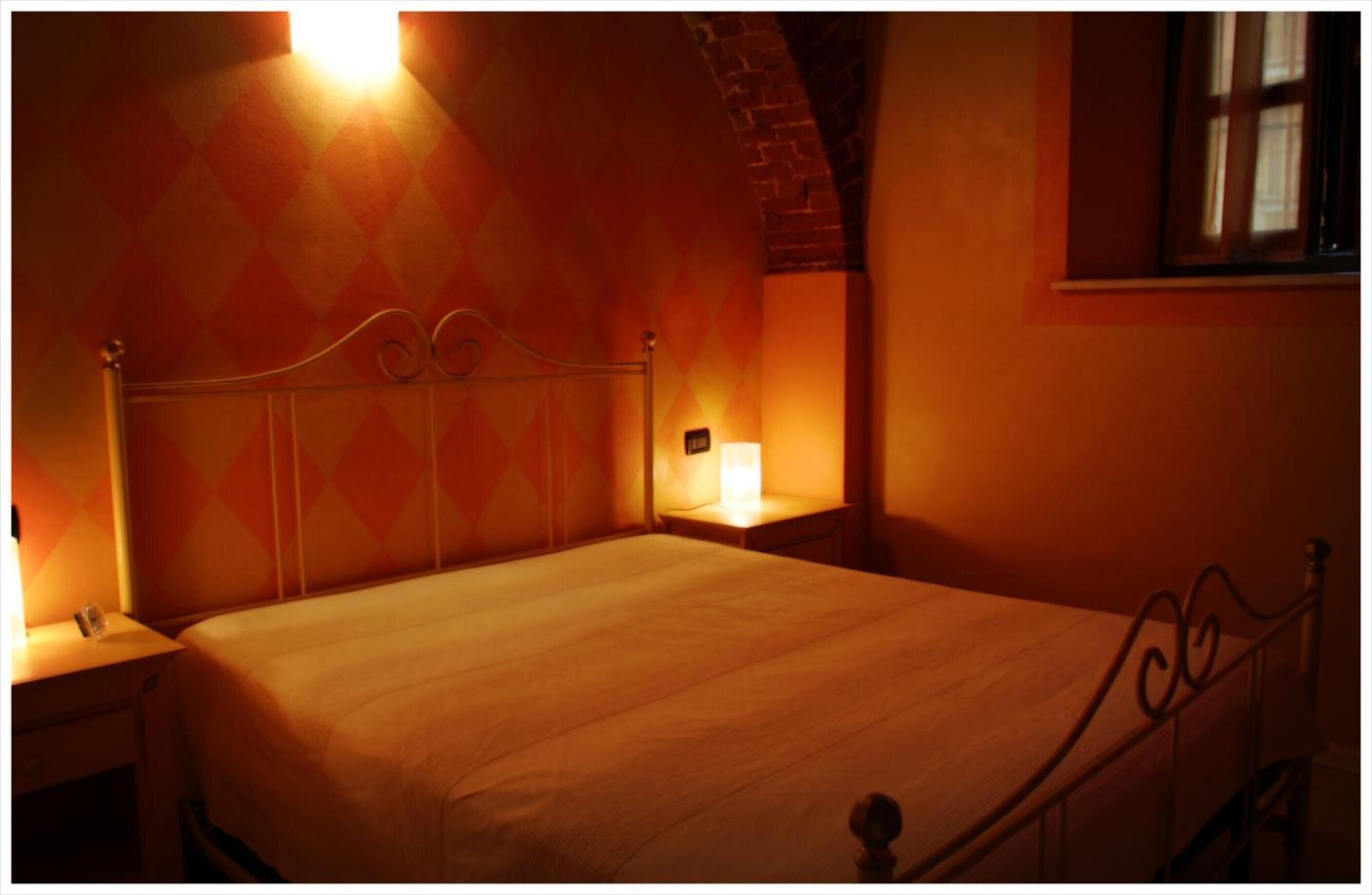 Ein Einzelbett mit Metallgestell in einem Raum mit gemustertem Wandpapier und einer Ziegelwand.