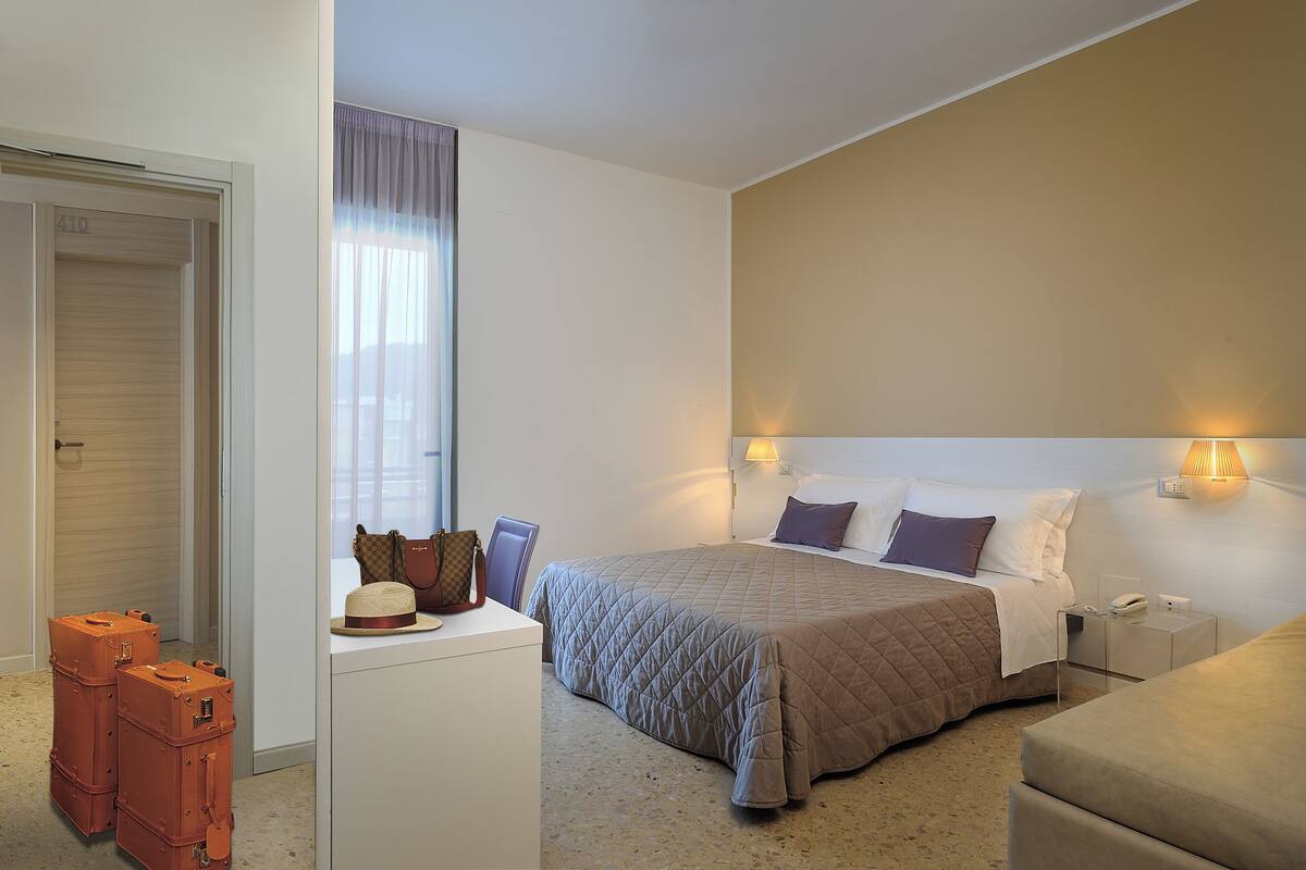 A hotel room with a bed, bedside tables, a desk, and a wardrobe.
