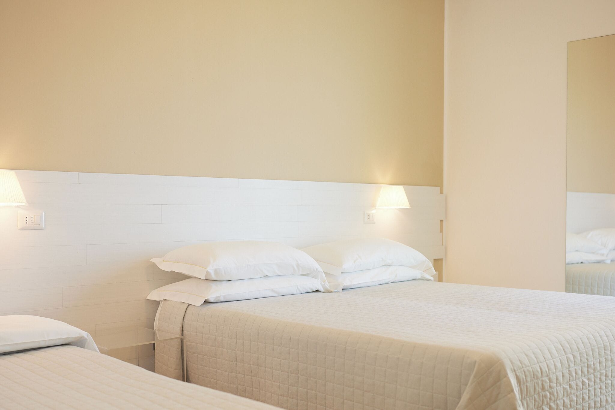 Une chambre d’hôtel avec deux lits, du linge de lit blanc et des lampes fixées au mur.