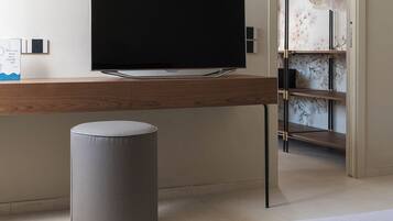 A bedroom with a bed, a desk with a flat-screen TV, a grey trash bin, and a wardrobe with a floral design.
