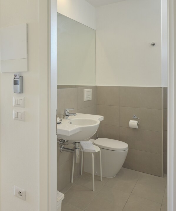 Un baño moderno con lavamanos, inodoro y un taburete pequeño.