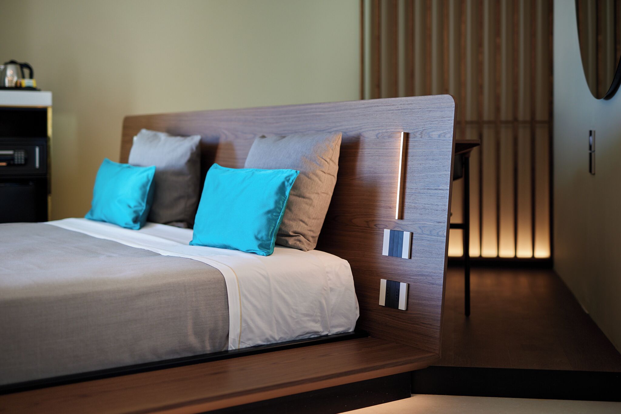 Uma cama moderna com cabeceira de madeira, duas almofadas e uma mesinha de cabeceira com chaleira.
