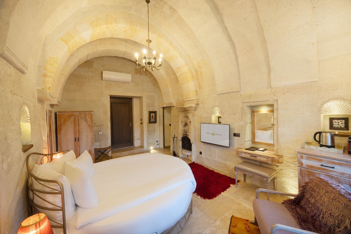 A spacious bedroom with a large bed, a sitting area with a red rug, a television, and a fireplace.