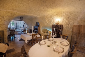An underground dining area with rustic stone walls, wooden furniture, and a white table set for a meal. - Tafoni Houses Cave Hotel (Ürgüp)