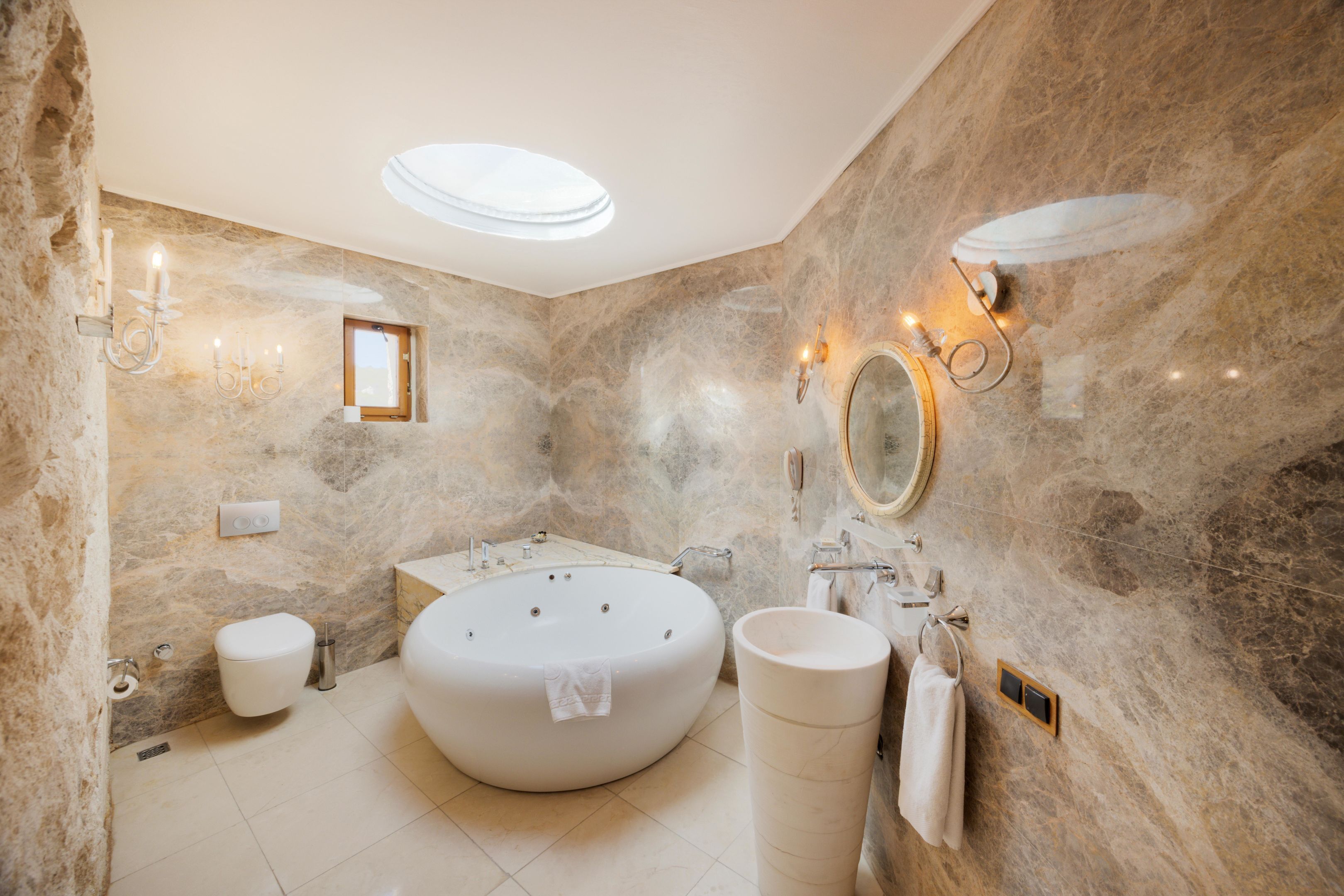 A bathroom with a freestanding bathtub, a round mirror, and a wall-mounted vanity.