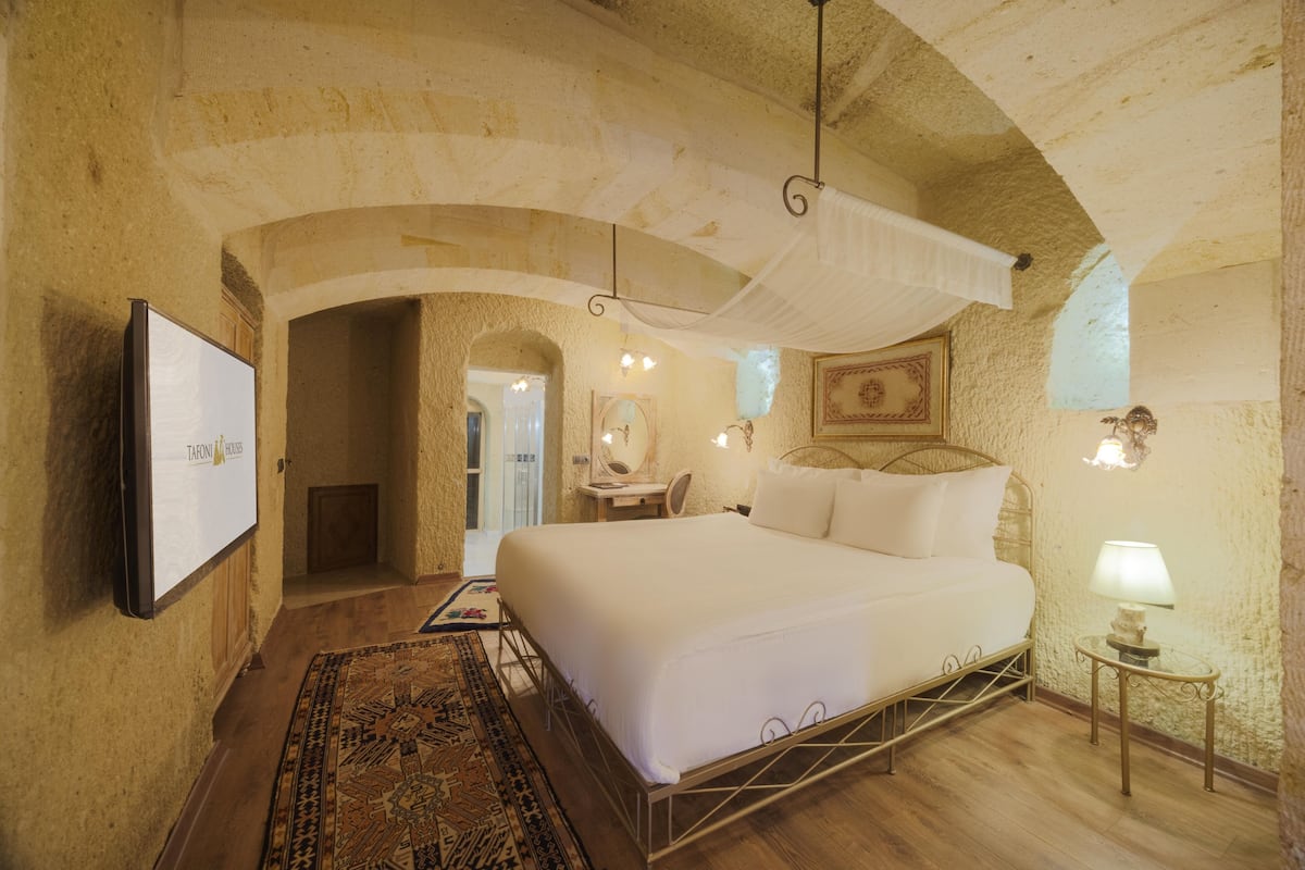 A bedroom with a large bed, a television on the wall, a small table with a lamp, and a patterned rug.