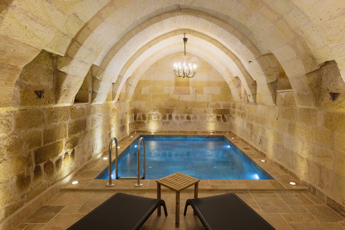 An indoor swimming pool with stone walls and a wooden table in the center.