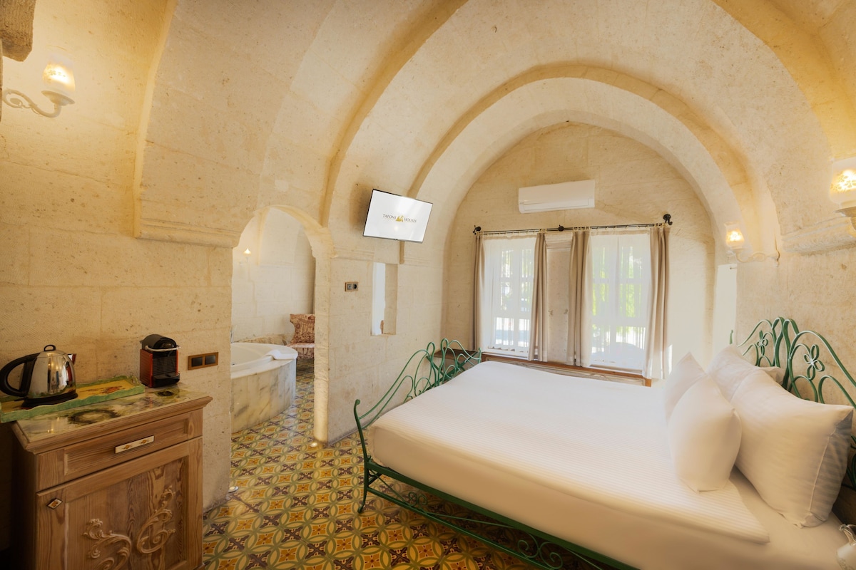 A bedroom with a bed, a TV, a window with curtains, and a tiled floor.