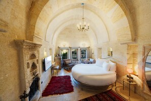 A spacious bedroom with a large bed, a chandelier, and stone walls. - Tafoni Houses Cave Hotel (Ürgüp)