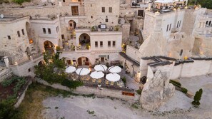 A traditional stone building with multiple levels, outdoor seating areas with umbrellas, and a courtyard. - Tafoni Houses Cave Hotel (Ürgüp)