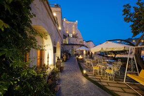 A courtyard with outdoor seating, stone pathway, and a historic building in the background. - Tafoni Houses Cave Hotel (Ürgüp)