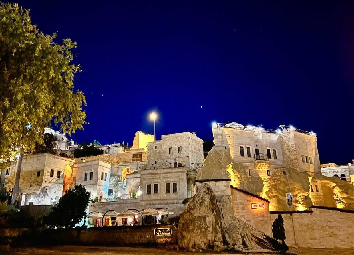 A historic building with stone architecture, illuminated by street lamps and lights, featuring a prominent entrance and a sign indicating a restaurant.
