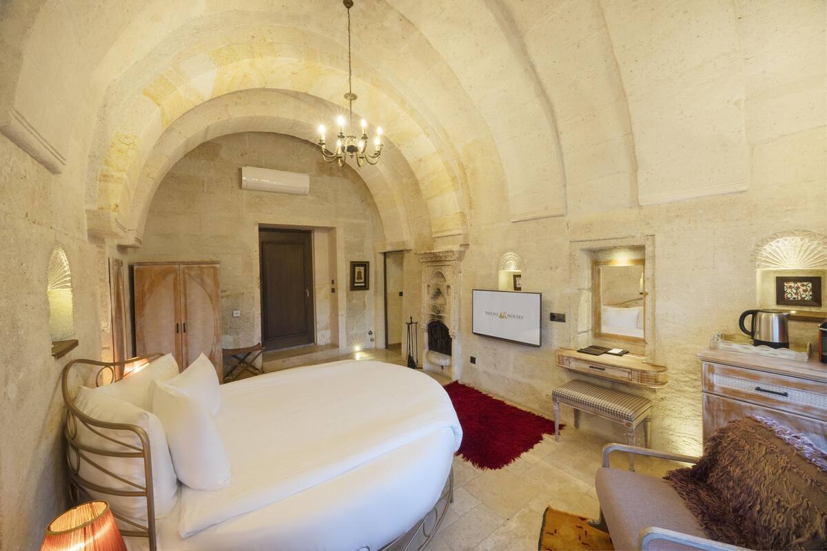 A bedroom with a large bed, a TV, a fireplace, and a stone archway.