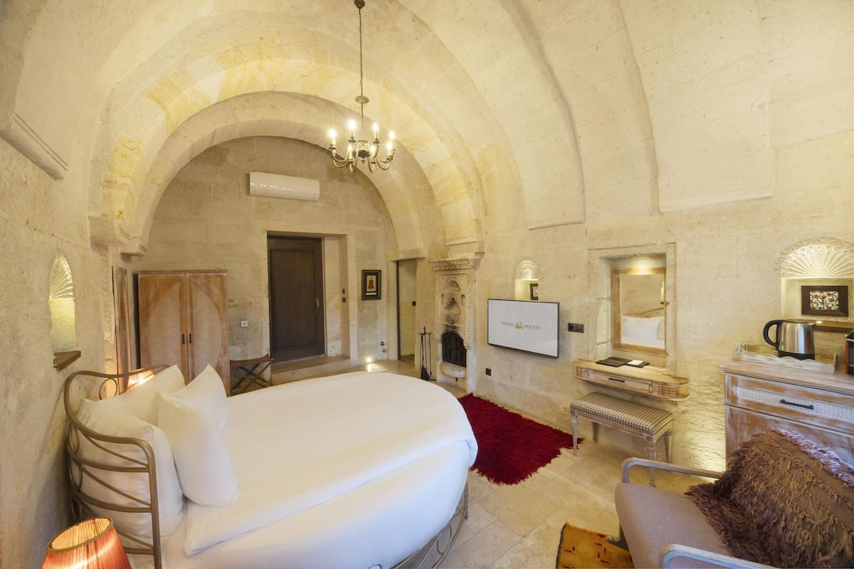 A bedroom with a large bed, a TV, a fireplace, and a stone archway.