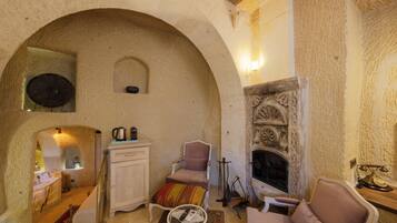 Un interior acogedor con un arco de piedra, una chimenea, un gabinete blanco, un sillón mullido y una pequeña mesa con un control remoto.
