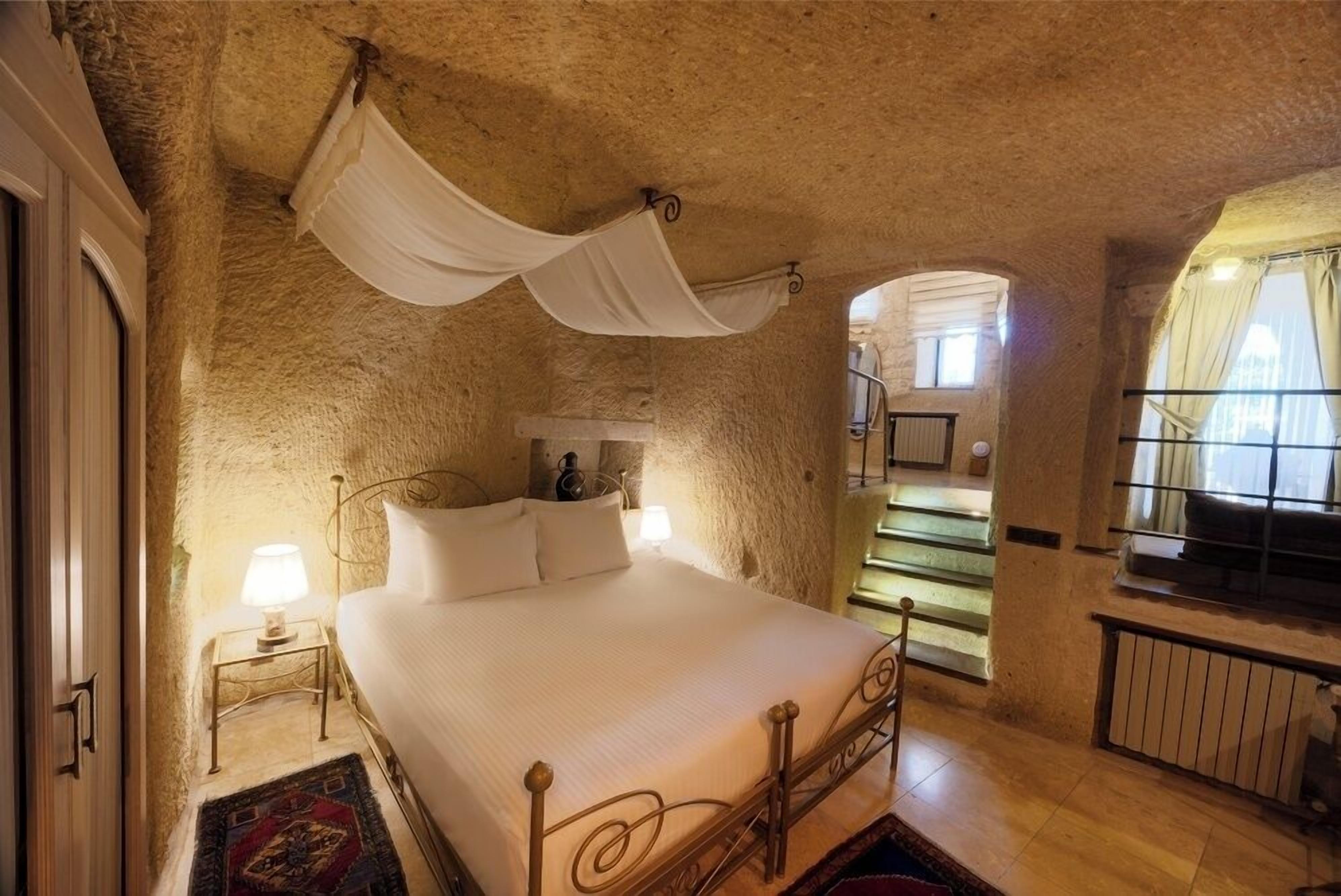 A bedroom with a bed, a nightstand, a window with curtains, and a staircase.