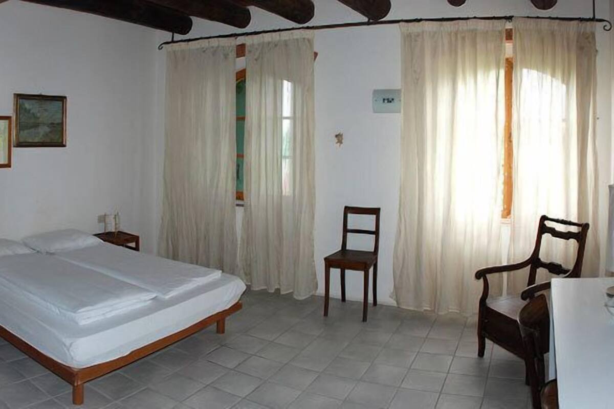 A bedroom with a large bed, two chairs, a bedside table, and a mirror.