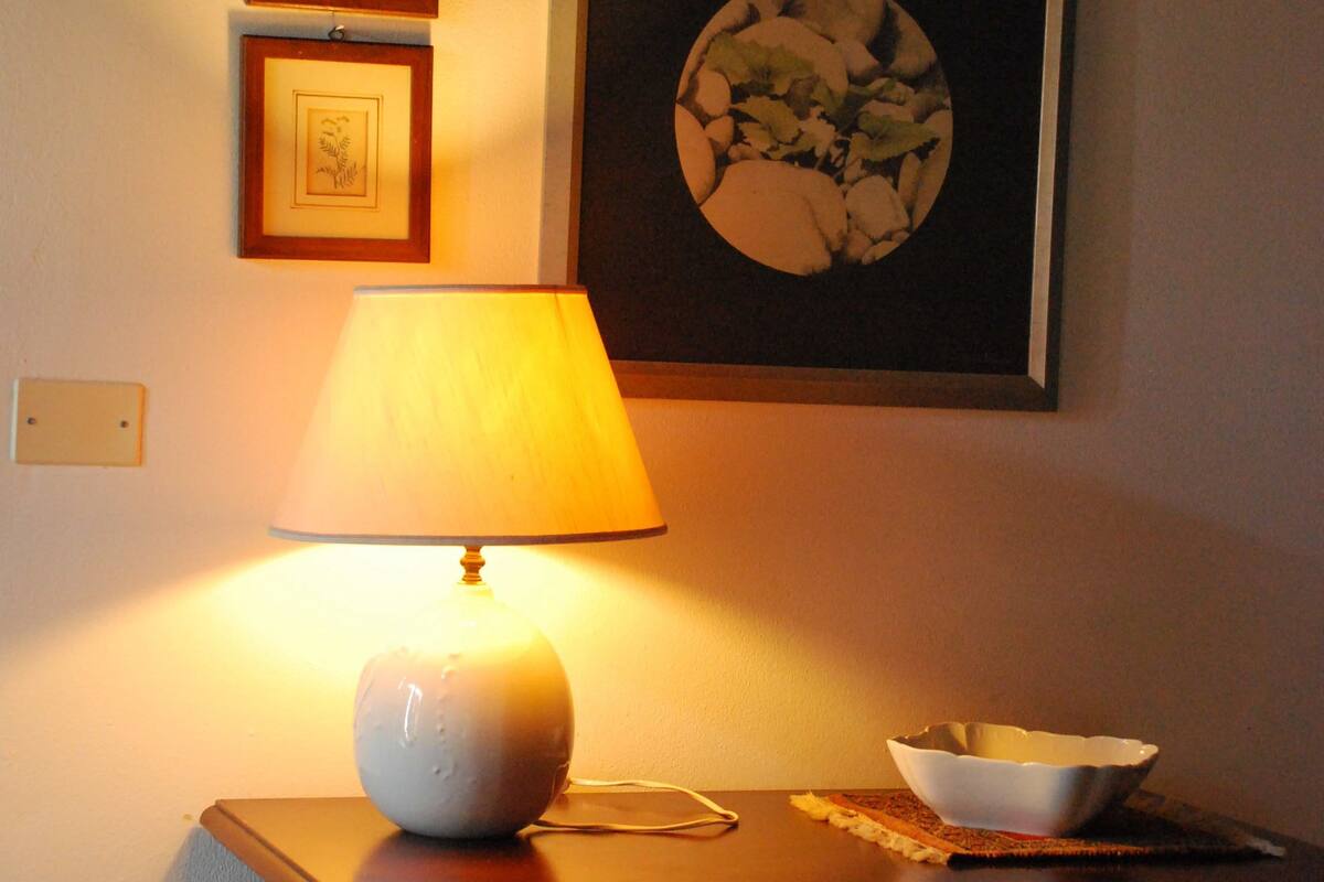 A table with a lamp, a bowl, and framed pictures on the wall.