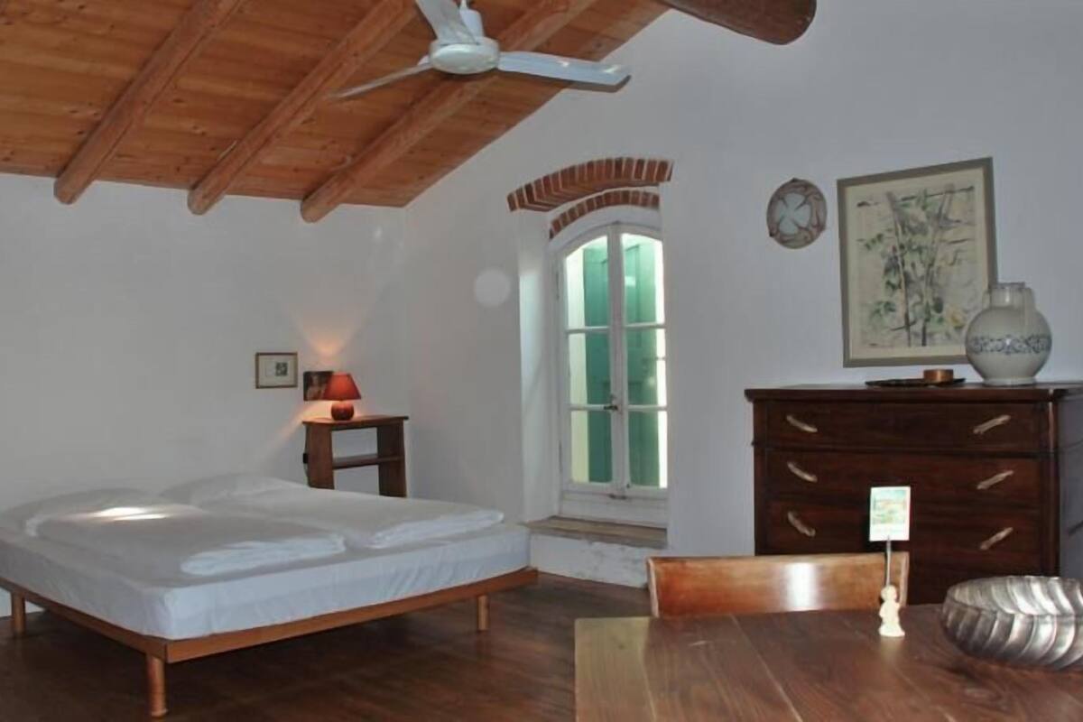 A bedroom with a wooden ceiling, a bed, a dresser, a window, and a small table.