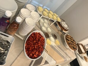 A buffet table with various food items including a bowl of strawberries, a pie, and several containers of condiments. - Hotel Excelsior (Gabicce Mare)