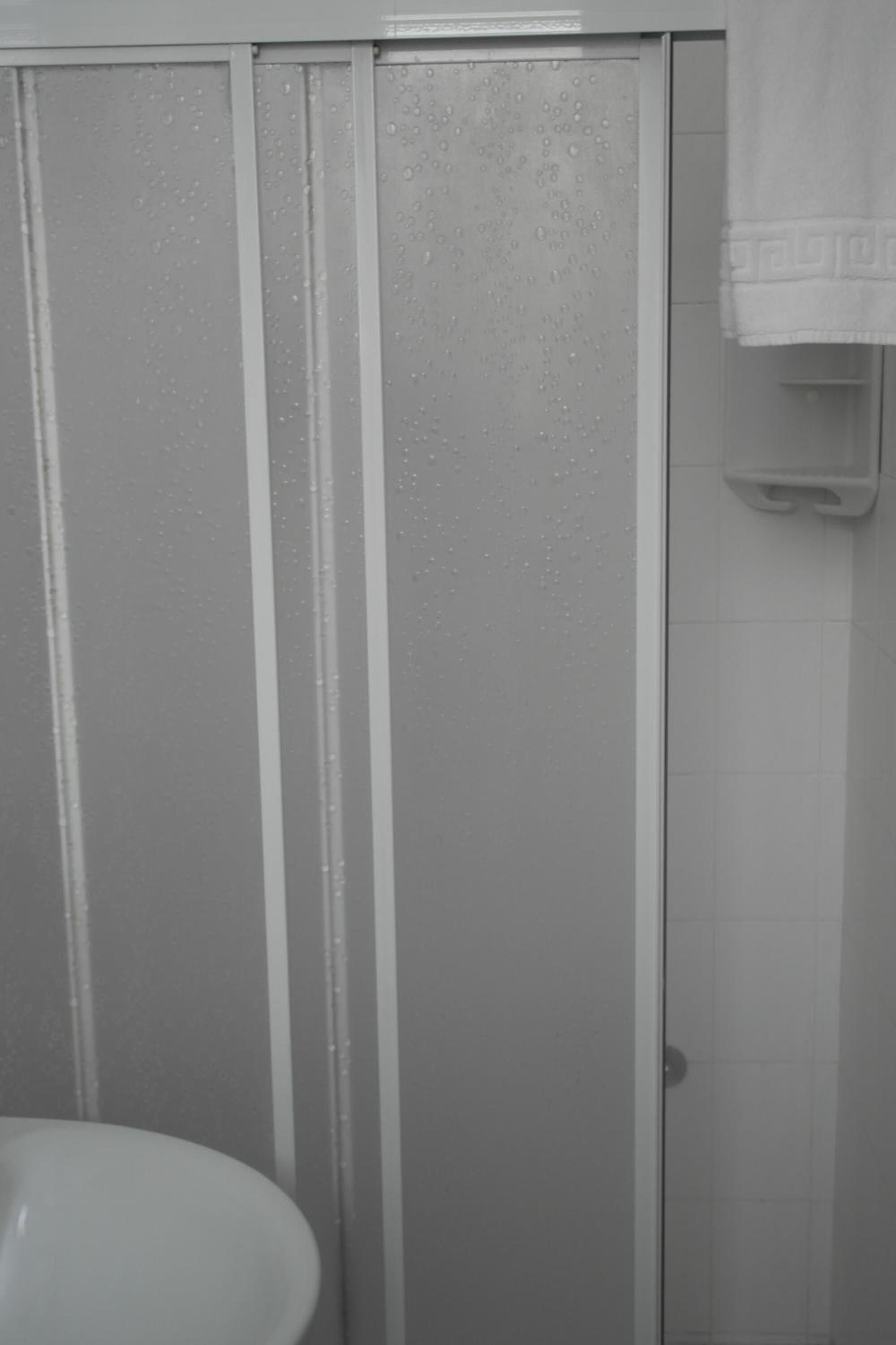 A bathroom with a shower enclosure, a sink, and a towel hanging on the wall.