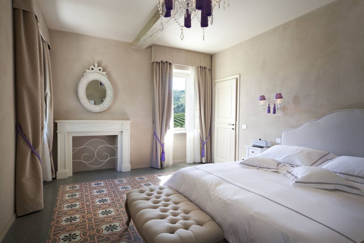 Un dormitorio con una cama grande, chimenea, espejo y vistas al exterior.