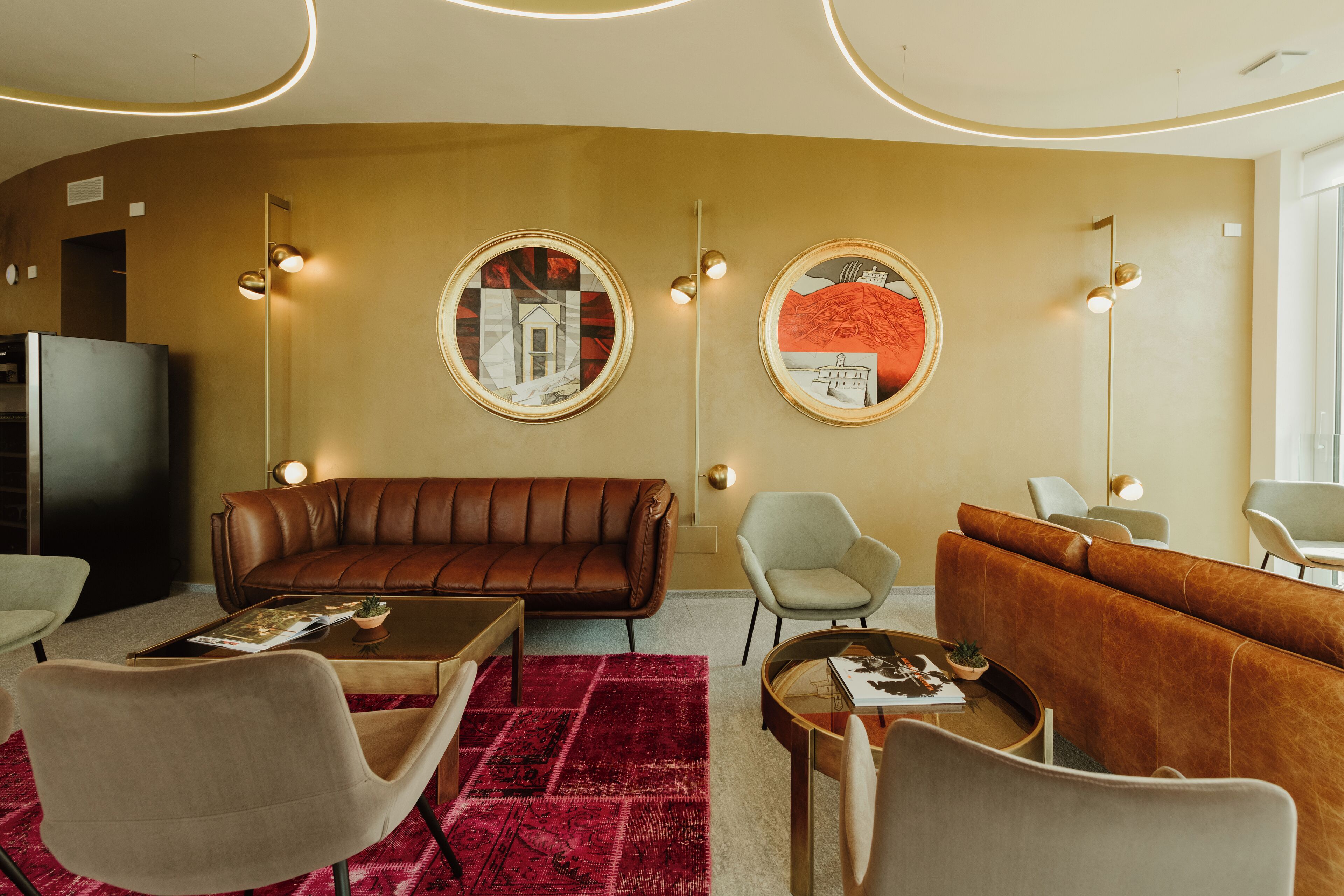 A modern living room with a brown leather sofa, a grey armchair, and a red patterned rug. There are two wall-mounted round mirrors and a tall floor lamp.