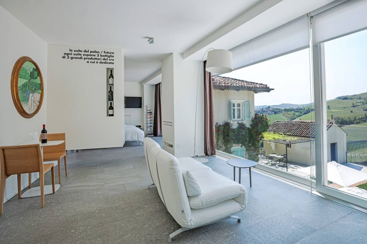 Una sala de estar moderna con un ventanal amplio, un sofá, un comedor con mesa y sillas, y vistas a un viñedo.