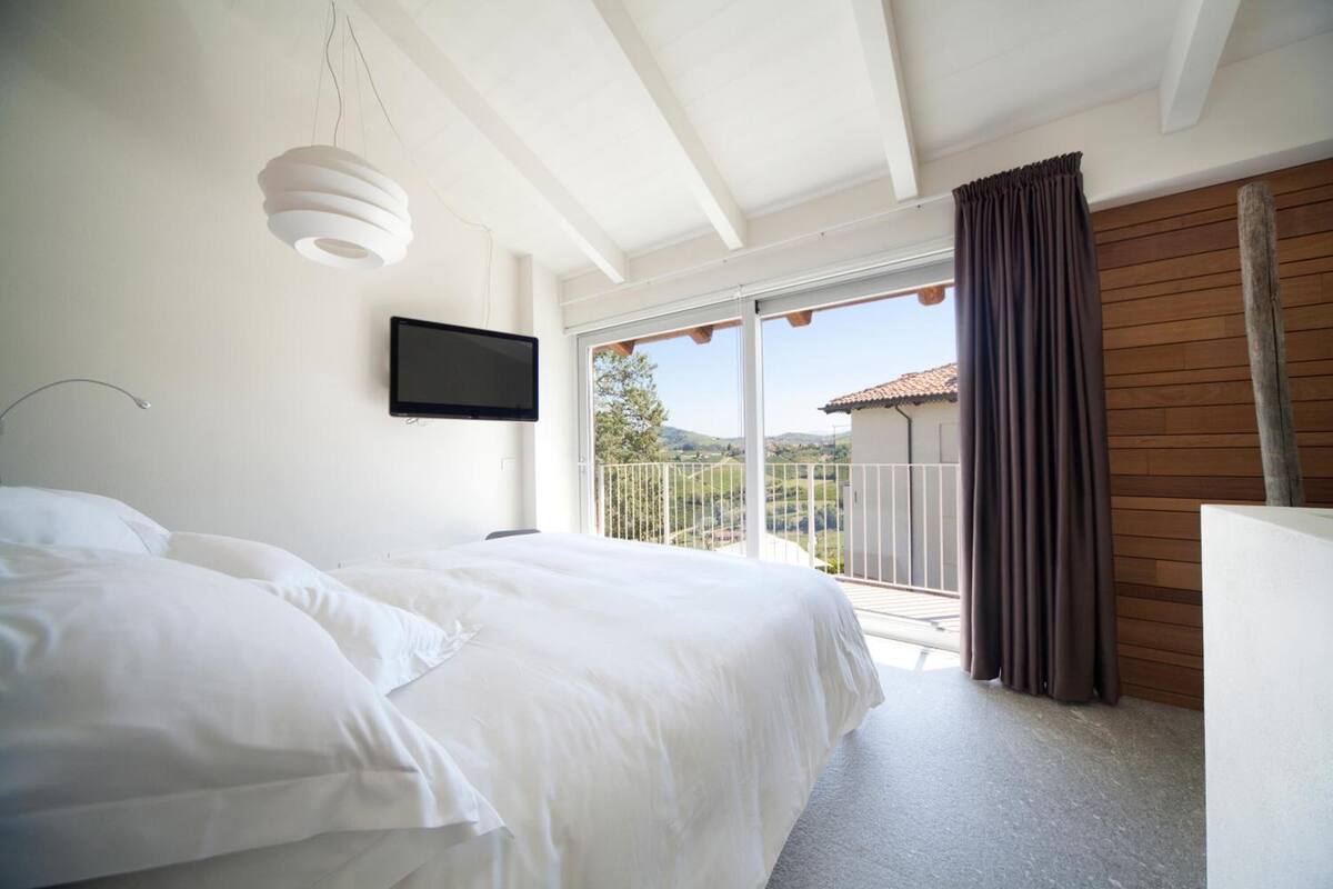 Un dormitorio con una cama grande, un televisor montado en la pared y un balcón con vistas al campo.