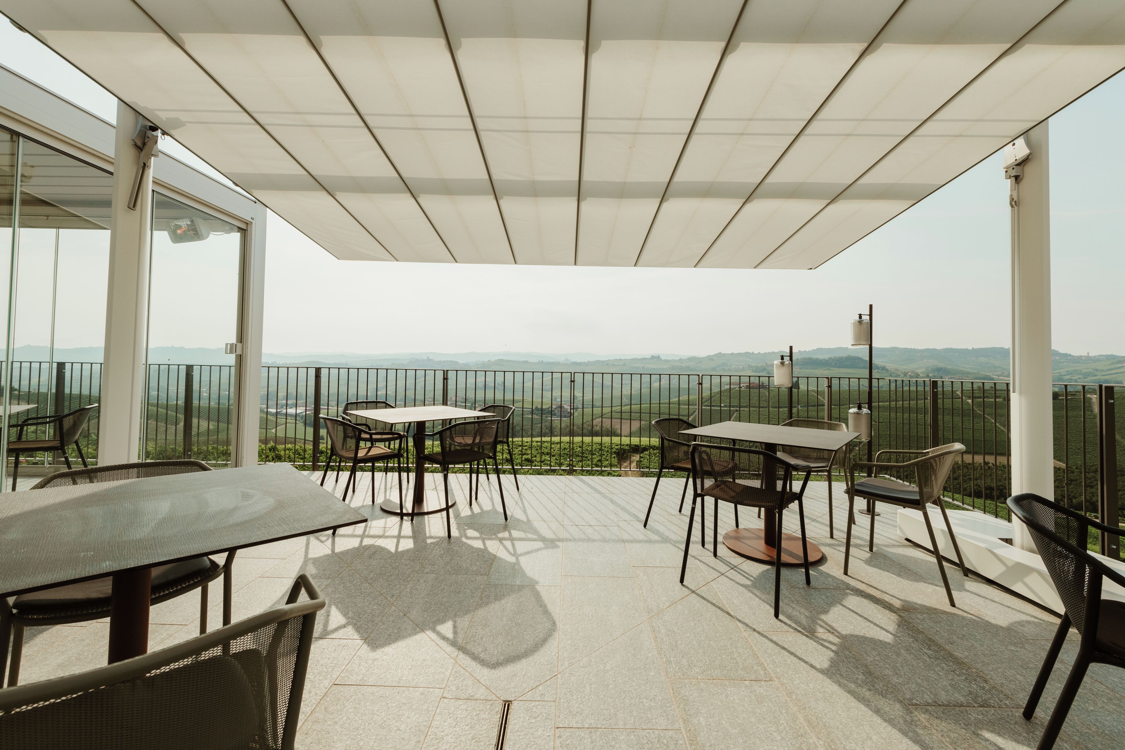Un patio techado al aire libre con una mesa y sillas, con vistas a colinas distantes.