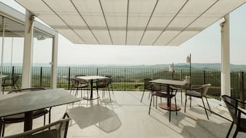 A covered outdoor patio with a table and chairs, offering a view of distant hills.