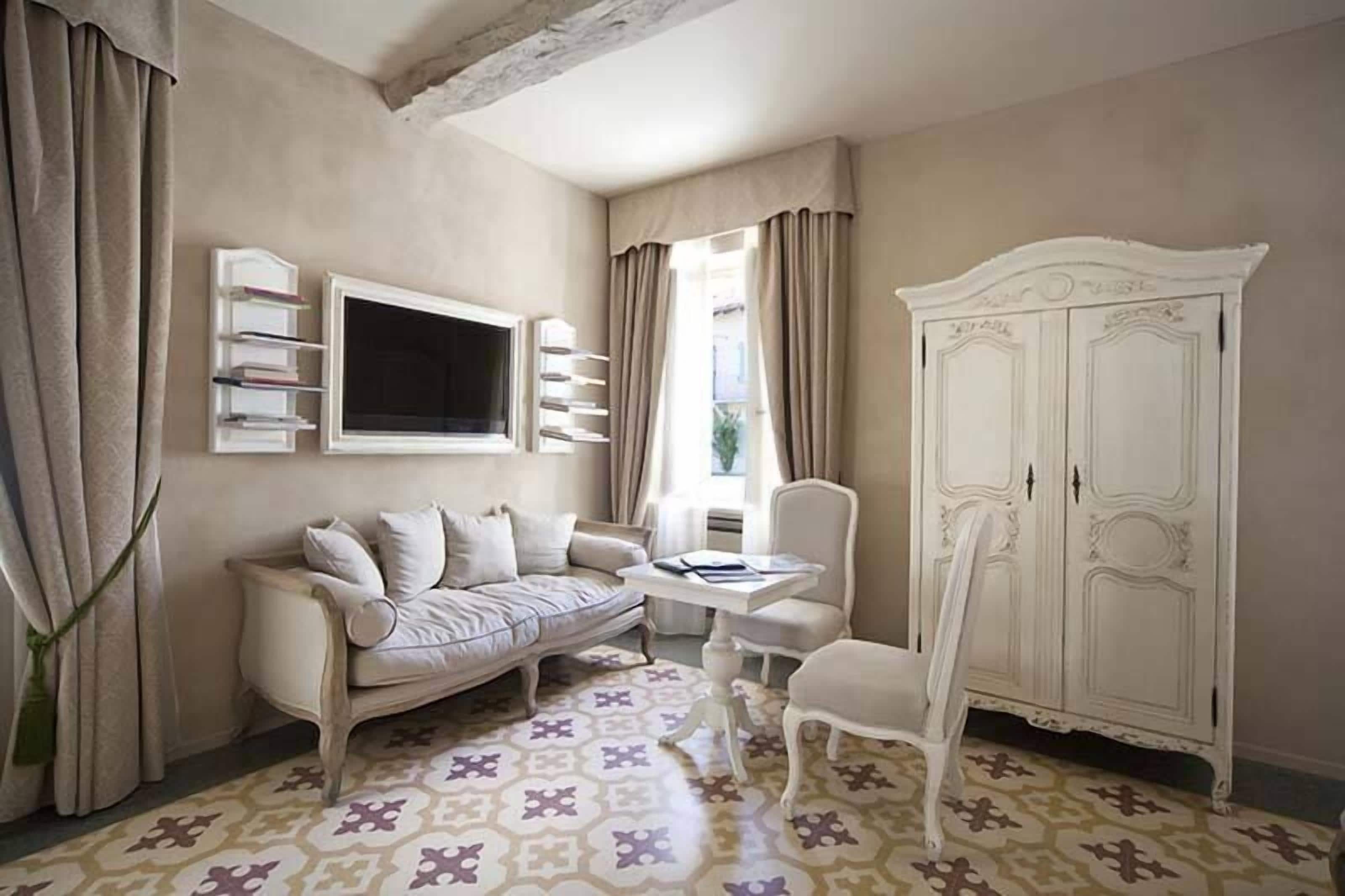 A room with a sofa, a small table, a chair, a wardrobe, and a TV mounted on the wall.