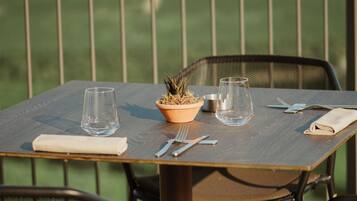 A table set outdoors with a potted plant, two glasses, cutlery, and a napkin.