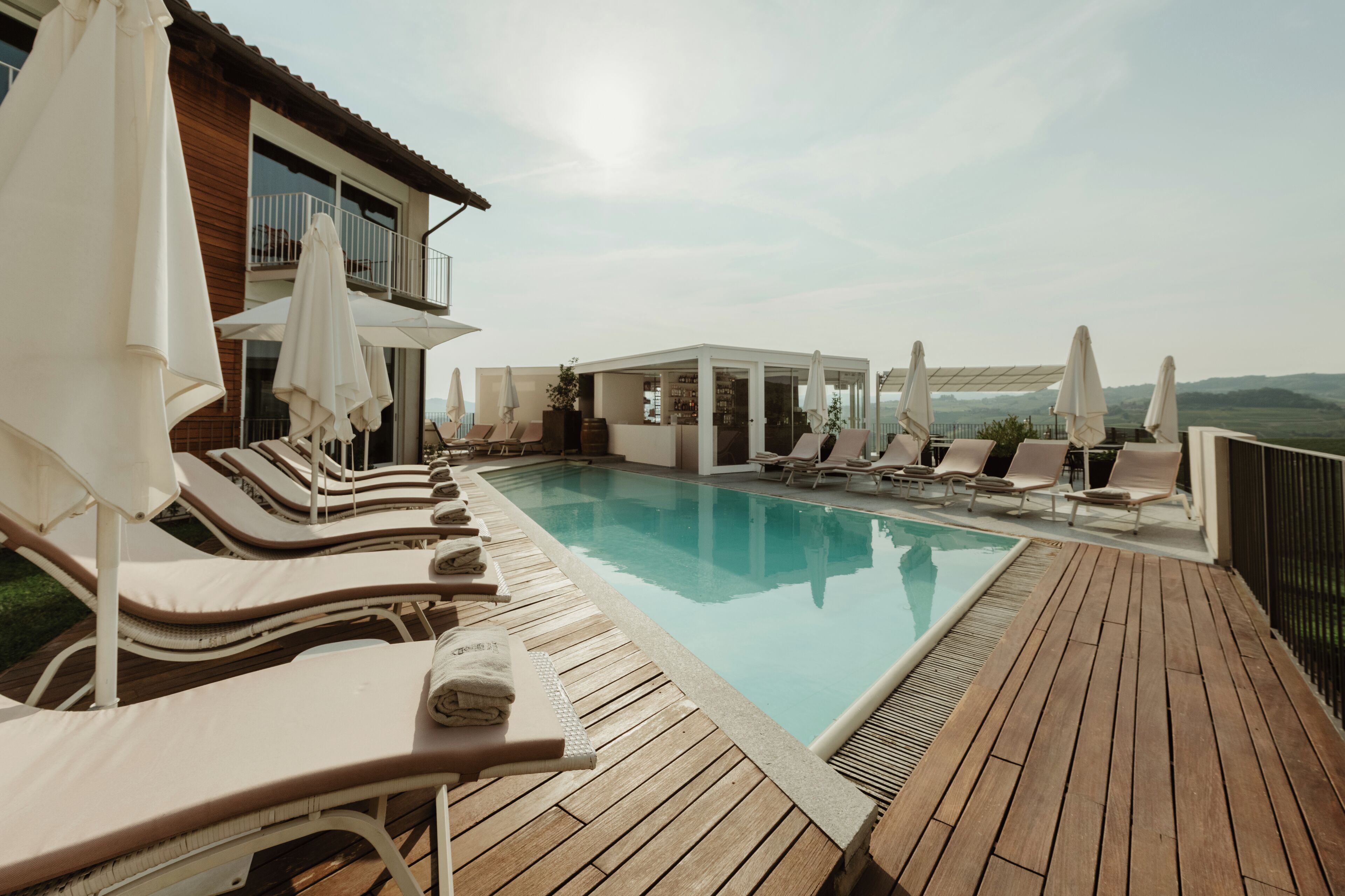A poolside area with lounge chairs and umbrellas, a wooden deck, and a view of the landscape.