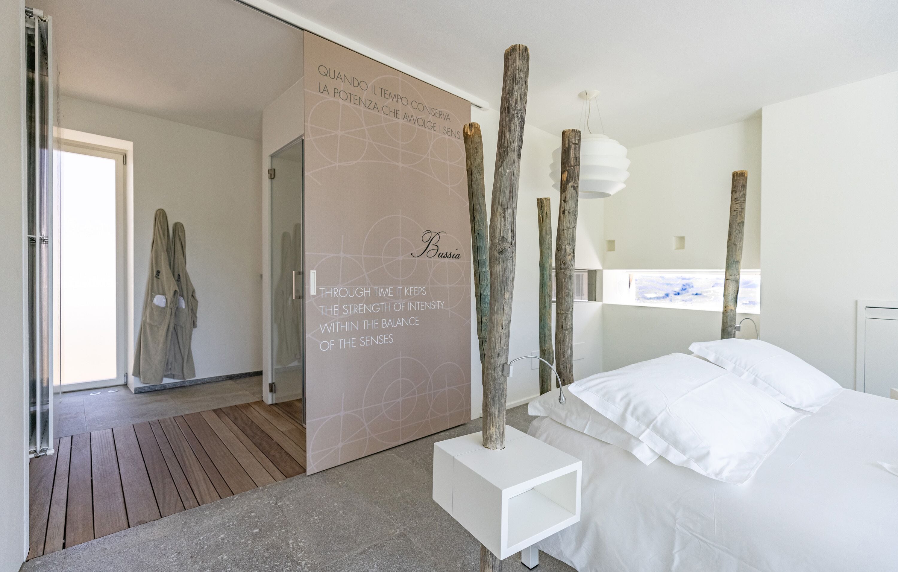 A modern bedroom with a large bed, a white bedside table, and a wall with a motivational quote.