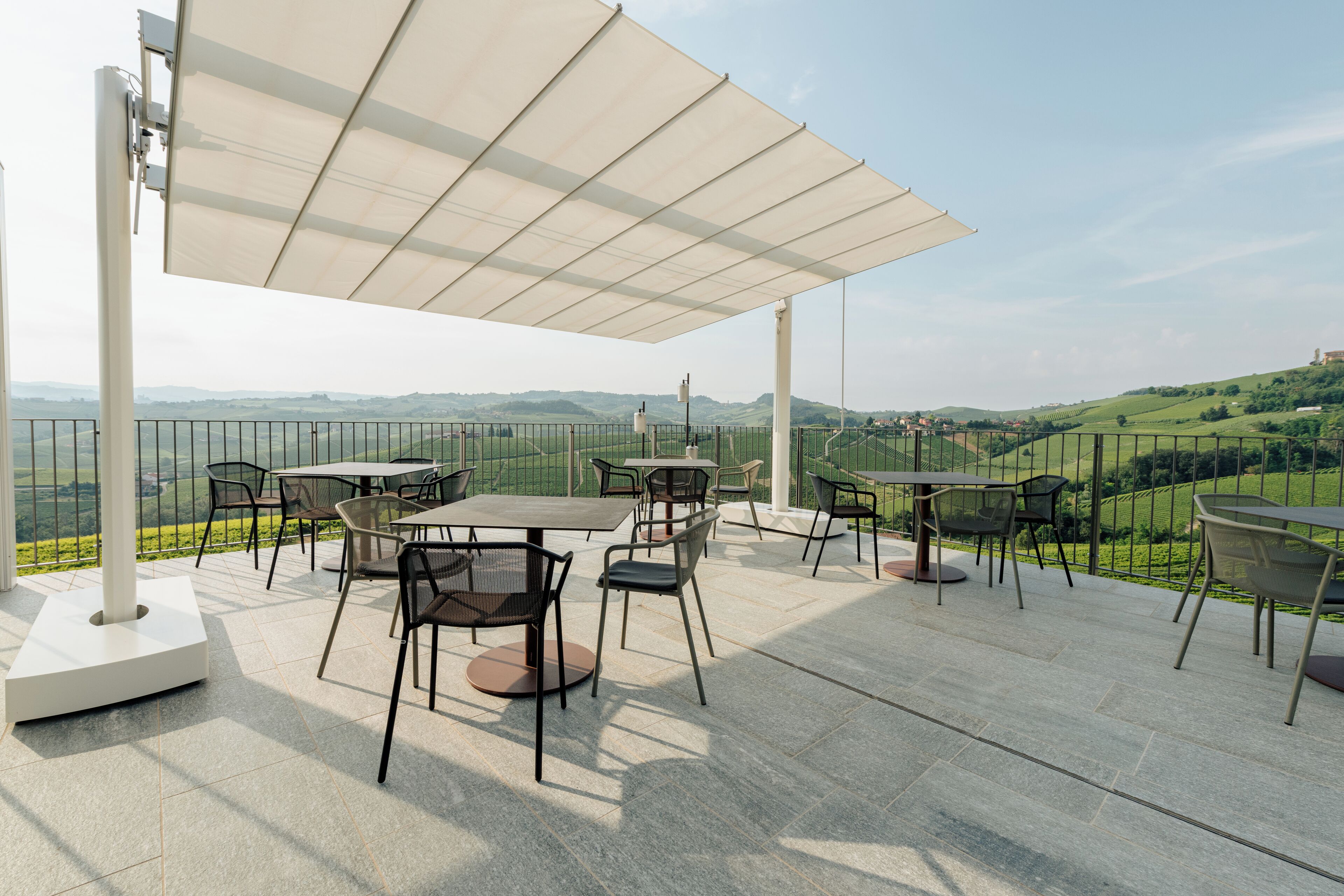 An outdoor patio with tables and chairs, a large canopy, and a scenic view of rolling hills.
