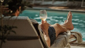 A person relaxing by a poolside lounge chair, holding a glass of white wine. - Palas Cerequio BaroloCruResort (Barolo)