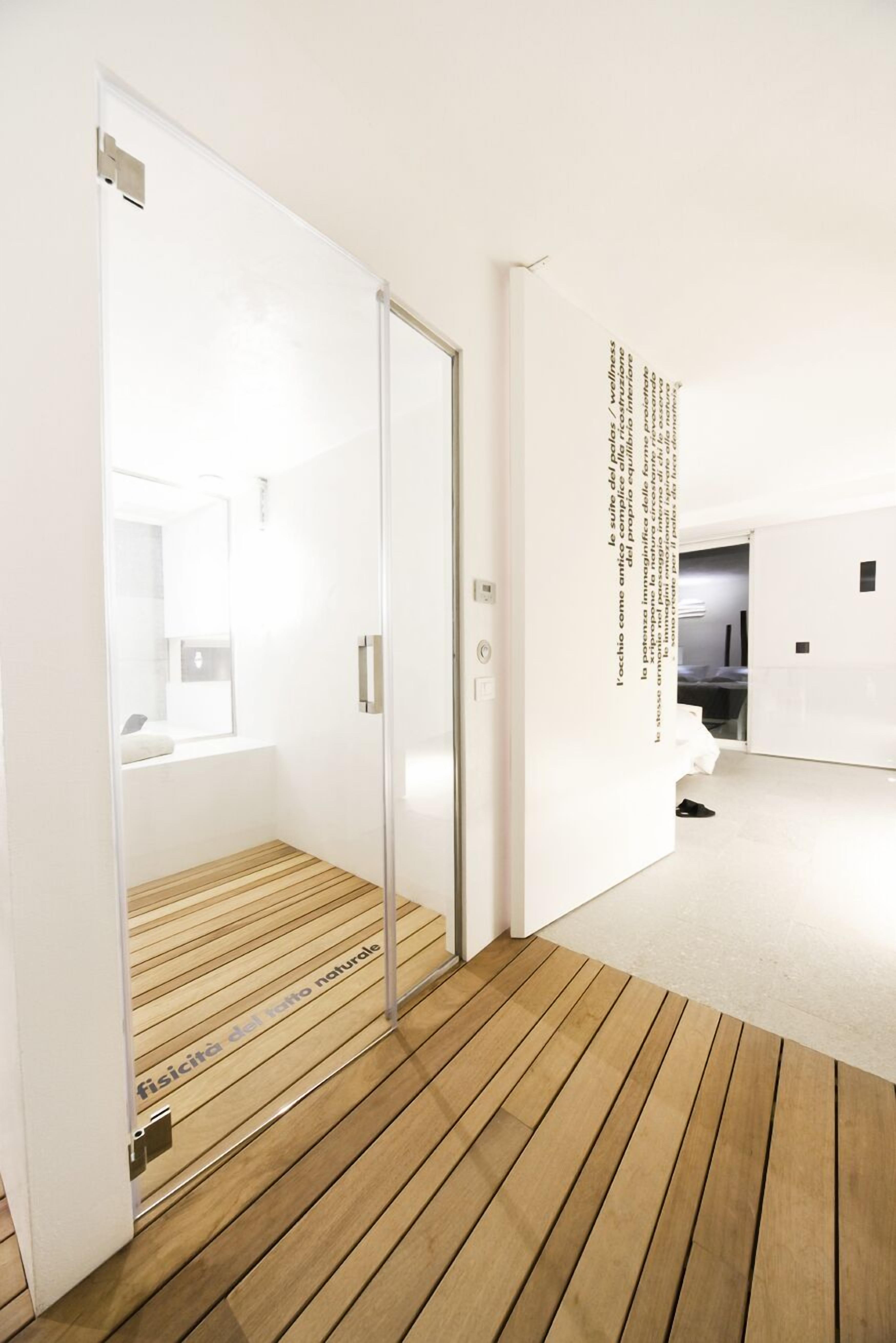 Una habitación de hotel moderna con suelo de madera, una puerta de vidrio que conduce a un baño y una pared con texto.