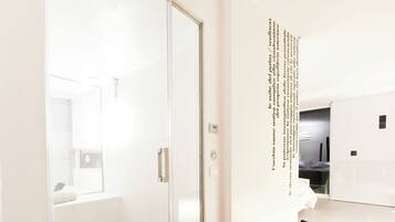 Una habitación de hotel moderna con suelo de madera, una puerta de vidrio que conduce a un baño y una pared con texto.