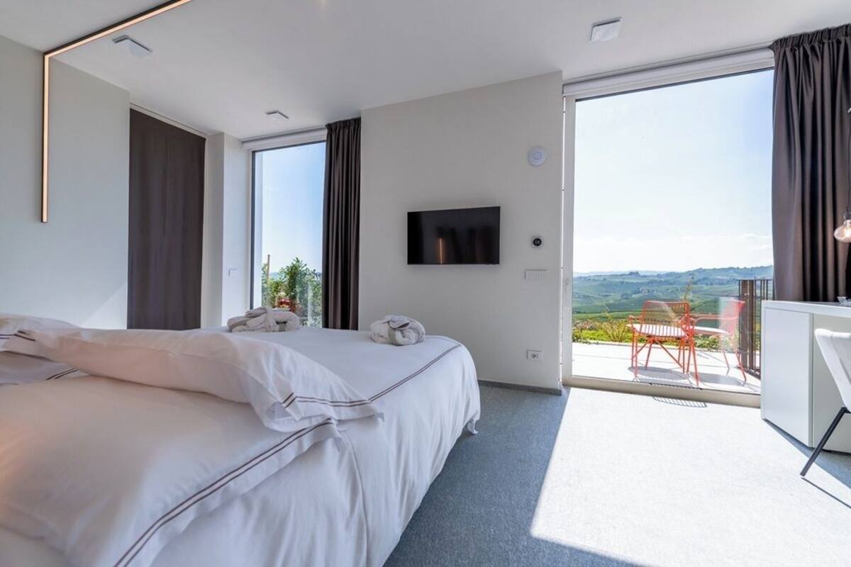 Una habitación de hotel moderna con una cama grande, una televisión de pantalla plana, un balcón con vistas y un escritorio con silla.