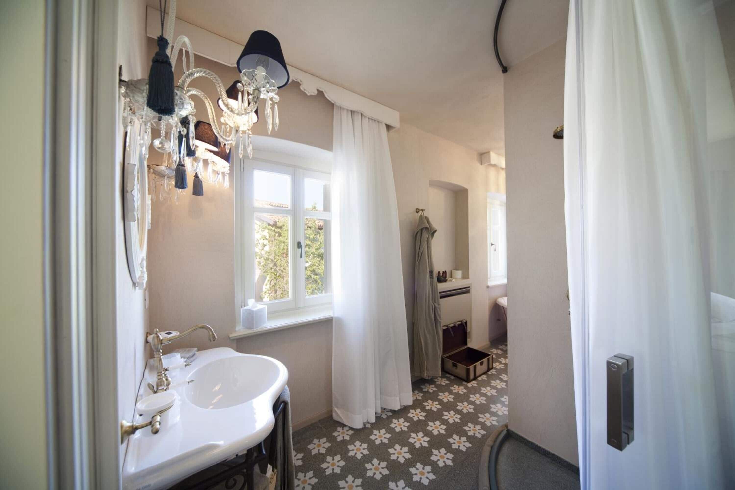 Un bagno con un lavandino bianco, un lampadario e una finestra con tende.