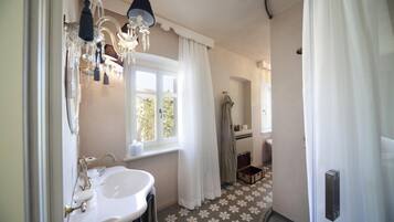 A bathroom with a white sink, a chandelier, and a window with curtains.