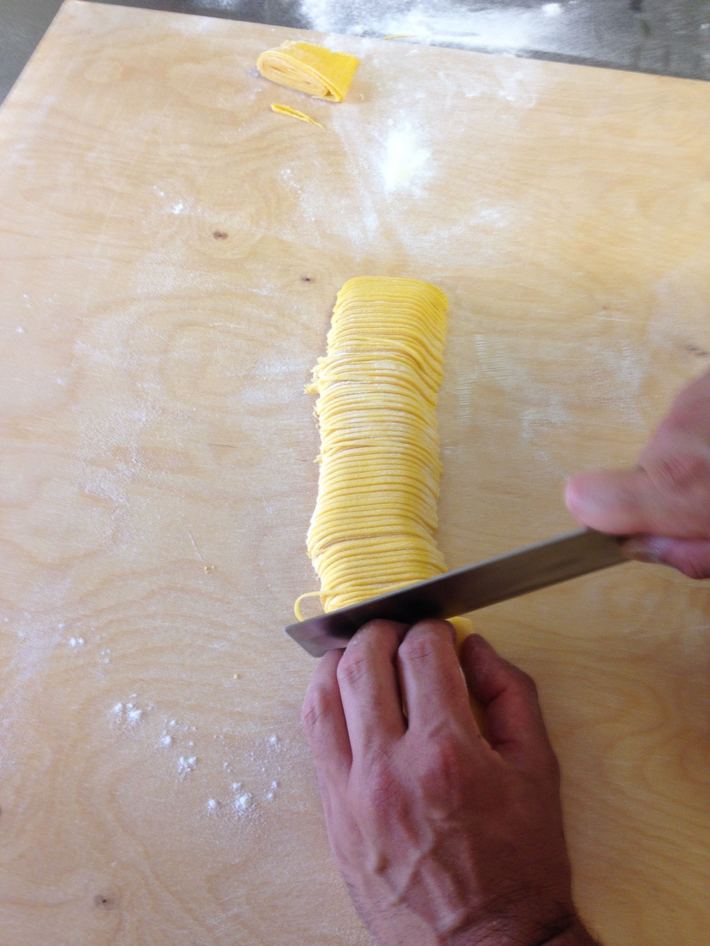 Una persona cortando un objeto largo y delgado de color amarillo sobre una superficie de madera.