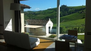 A modern room with a large window offering a view of a vineyard and distant hills. - Palas Cerequio BaroloCruResort (Barolo)