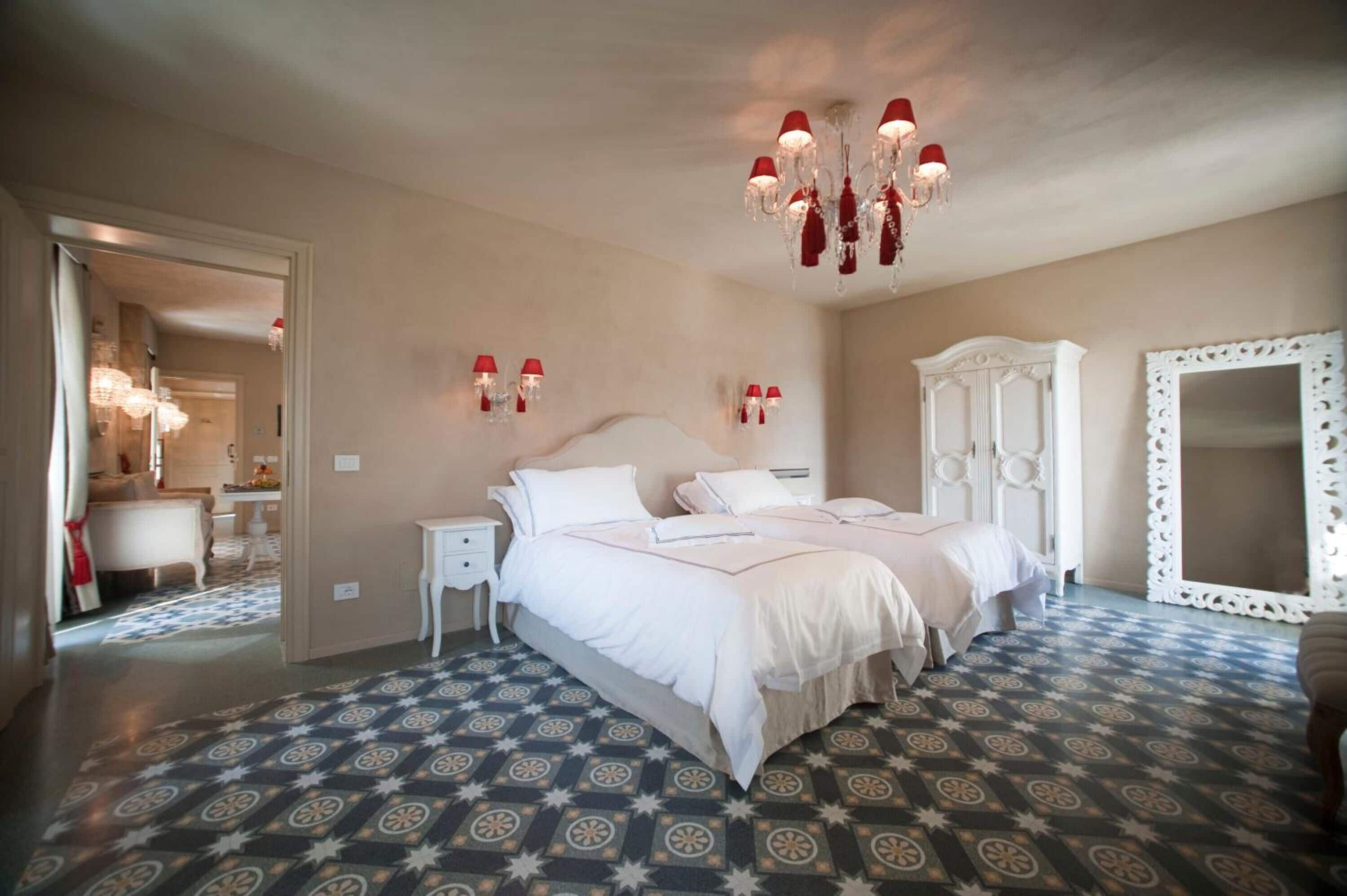 A bedroom with two beds, a chandelier, a mirror, and a patterned floor.