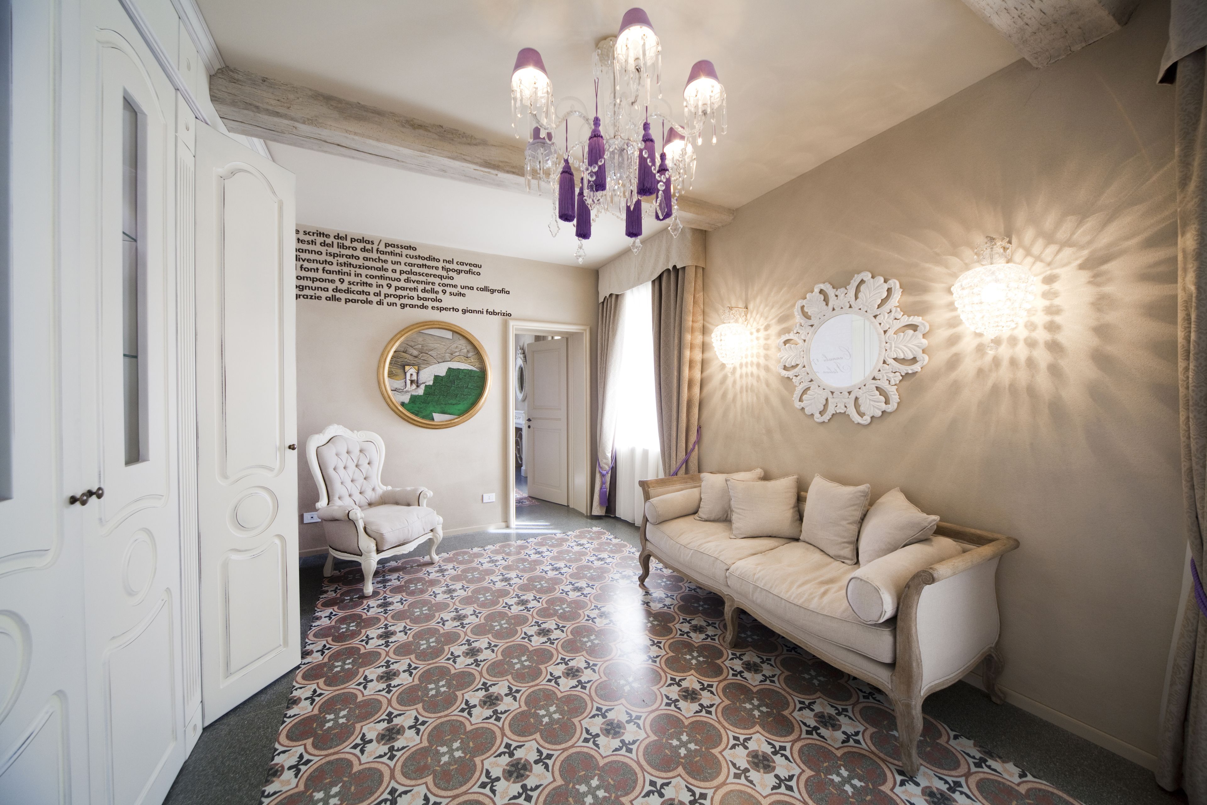 A room with a patterned floor, a beige sofa, a white armchair, and a chandelier.